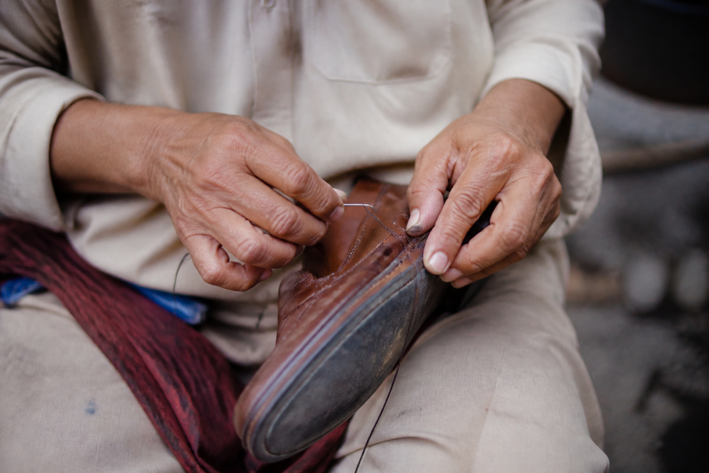 Mains tenant une chaussure brune avec fil et aiguille