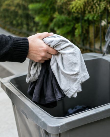 Main depose vetements usages dans bac gris